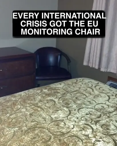 Photograph of an ugly black plastic chair in the corner of a darker room. Caption reads: Every international crisis got tye EU monitoring chair